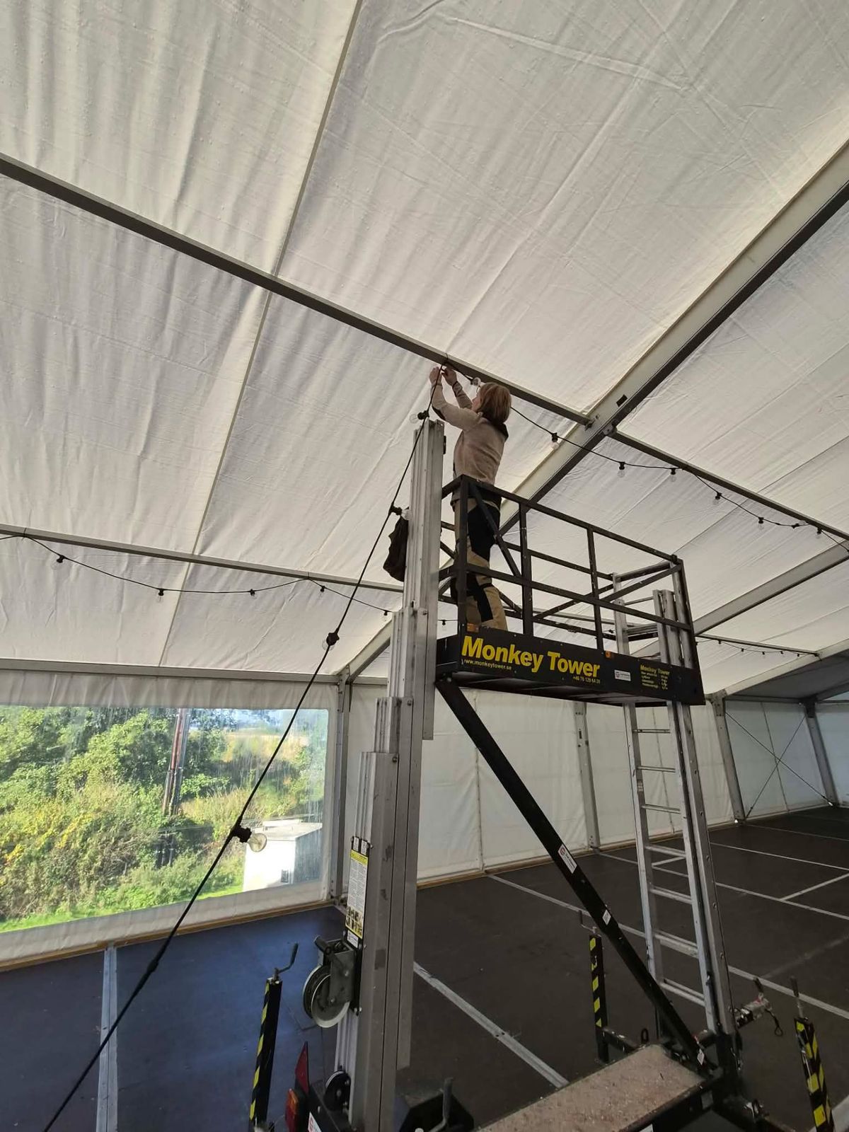 Medlem riggar ljusslingor i festivaltältet från en lift